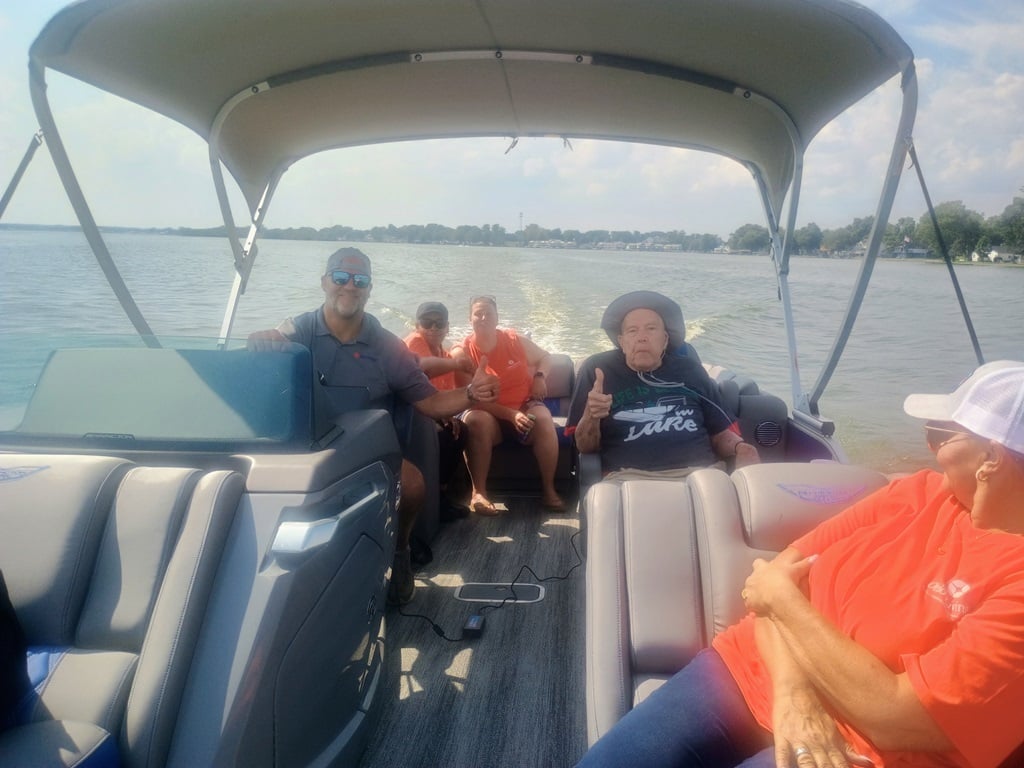 Older adult enjoys a sunny pontoon boat ride on the lake with several companions, including Ohio Living team members, while giving a thumbs-up from his seat.