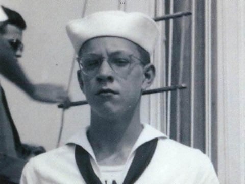 Black-and-white photograph of a young sailor wearing glasses and a traditional U.S. Navy uniform and white sailor cap.